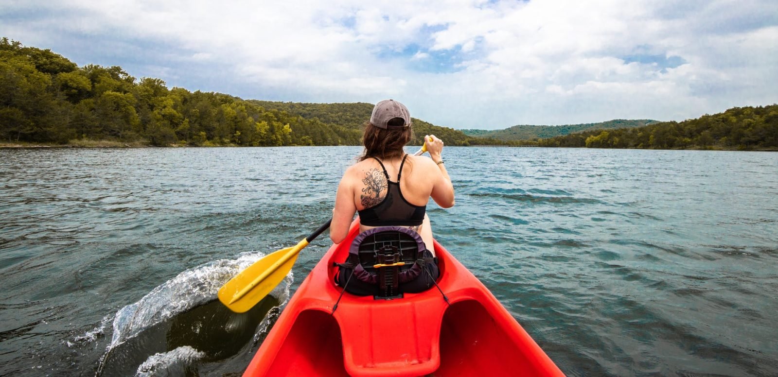 woman in black bikini top and brown hat sitting on red kayak