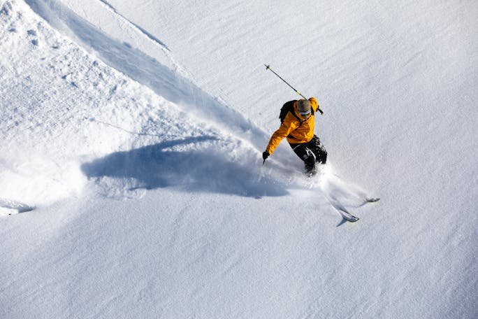 A skier in a yellow jacket skillfully glides down a snowy slope, showcasing athletic prowess.