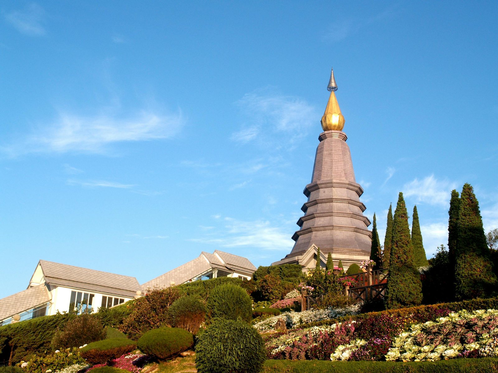 Beautiful view of a Buddhist pagoda surrounded by a vibrant garden in Chiang Mai, Thailand, under a clear blue sky.