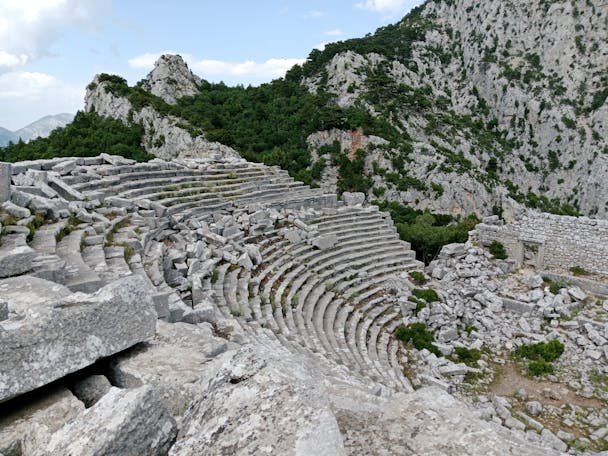 Ruins of an ancient amphitheater nestled within a rocky mountain landscape.